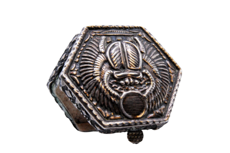 Caixa de comprimidos em prata de forma hexagonal com relevos na tampa basculante.